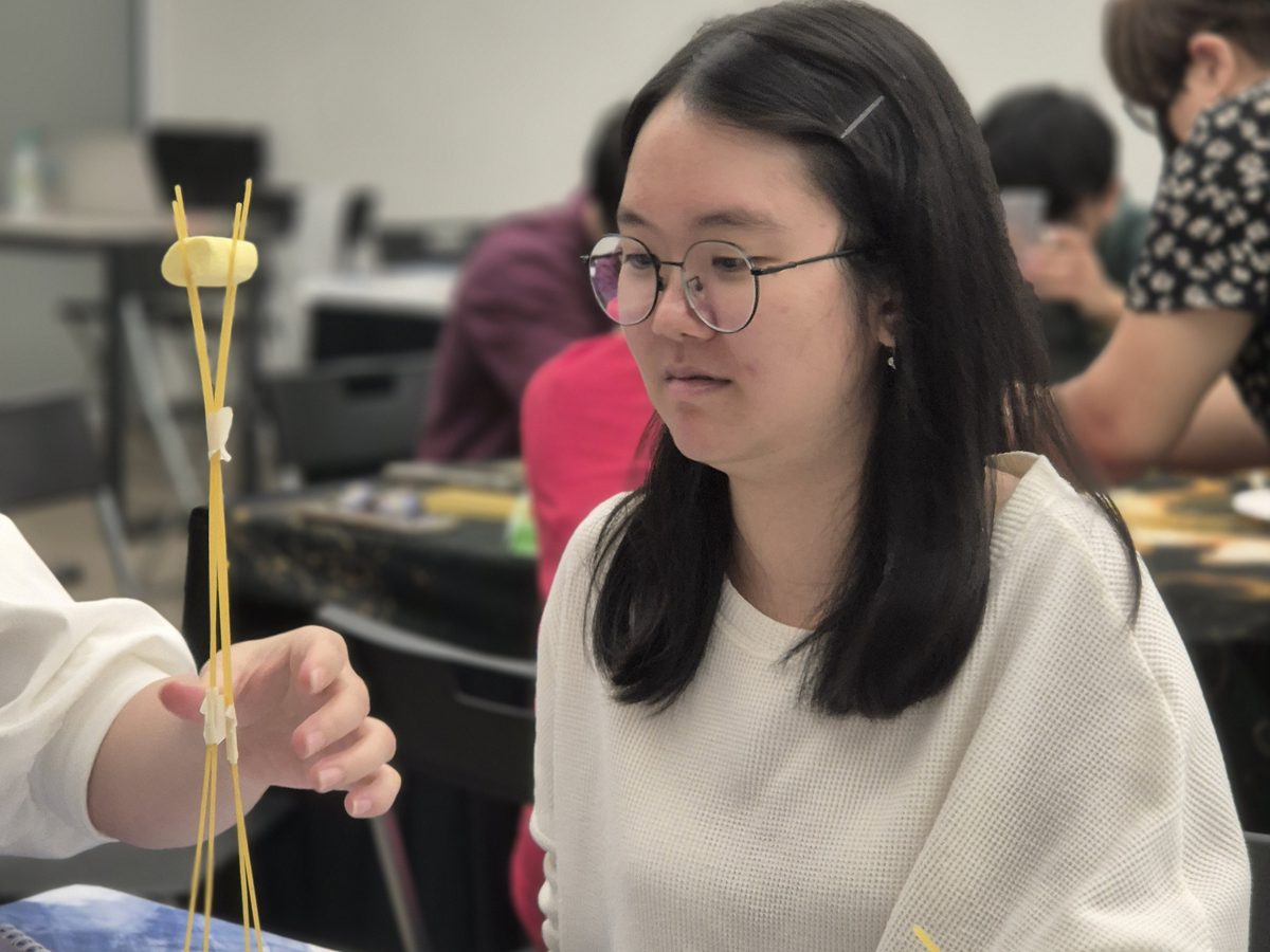 A participant steadying a spaghetti-and-marshmallow tower